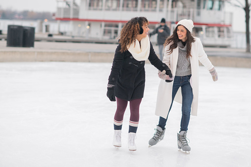 A gorgeous ethnic, female adult couple spend time together skating one afternoon. They are holding hands and smiling.