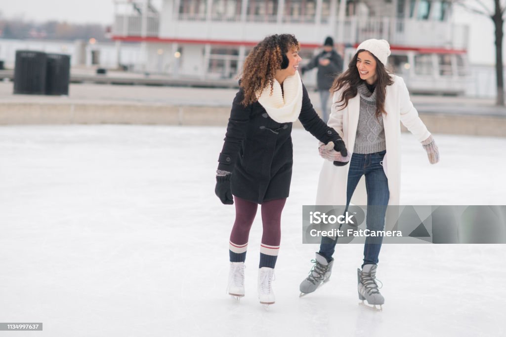 Adult Female Couple Ice Skating A gorgeous ethnic, female adult couple spend time together skating one afternoon. They are holding hands and smiling. Ice-skating Stock Photo