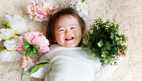 Happy toddler boy with spring flowers on a white carpet