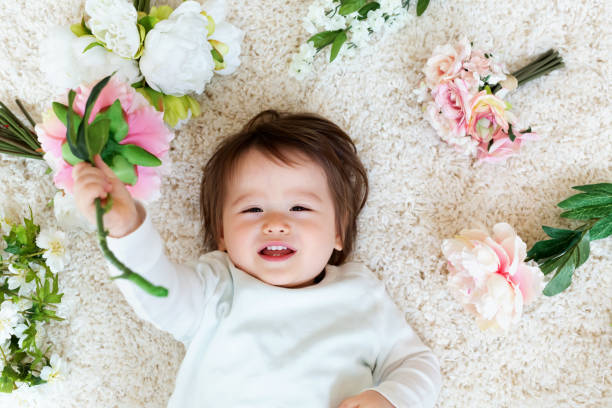 Happy toddler boy with spring flowers on a white carpet
