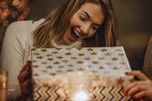 Portrait of a young woman opening a gift box and looking excited.
