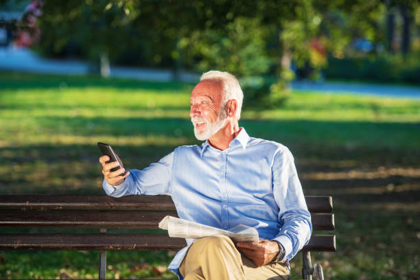 istock Smiling senior man talking on the phone while sitting on the bench in the park. 1135009221
