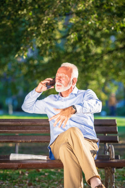 istock Smiling senior man talking on the phone while sitting on the bench in the park. 1135009235