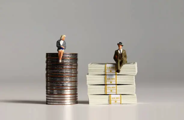 The concept of gender pay gap. A pile of bills and coins. Miniature people.