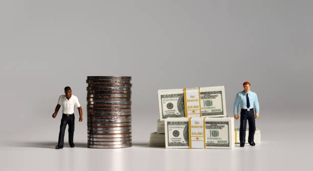 A pile of bills and coins. Miniature people. The concept of racial and income disparity. stock photo