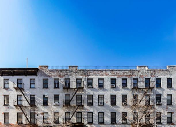 istock Panoramic view old white brick apartment building with windows and fire escapes and an empty blue sky background overhead in New York City 1135015201