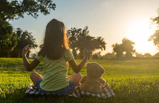 Little girl practicing yoga at sunset with her teddy bear.