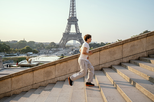 Sporty young man running up the stairs at the Eiffel Tower in Paris, France. People training sport in cities concept. Caucasian male sport training in morning at sunrise full of power and vitality