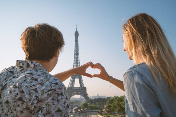 istock Young couple making heart shape finger frame with hands against the Eiffel Tower in Paris 1135026439