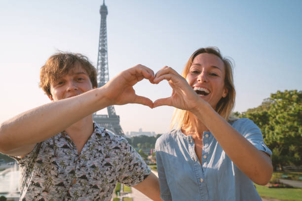 istock Young couple making heart shape finger frame with hands against the Eiffel Tower in Paris 1135028329