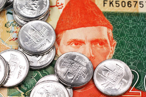 A twenty Pakistani rupee bank note with a pile of one rupee coins from Pakistan stock photo