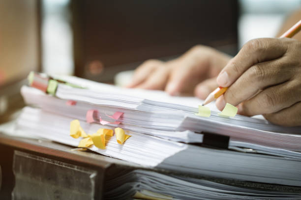 biznesmen ręce gospodarstwa ołówek pracy w stosy plików papierowych wyszukiwania niedokończonych dokumentów osiąga z dokumentów raportu biznesowego, praca zawodowa dla dokumentów finansowych na komputerze w biurze - lawyer research book finance zdjęcia i obrazy z banku zdjęć