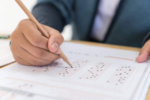 istock School Students hands taking exams, writing examination holding pencil on optical form of standardized test with answers sheet doing final exam in classroom. Education assessment Concept. Soft focus 1135034082