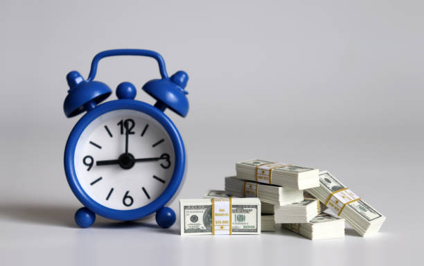 istock A blue alarm clock and a bunch of hundred dollar bills. 1135036961