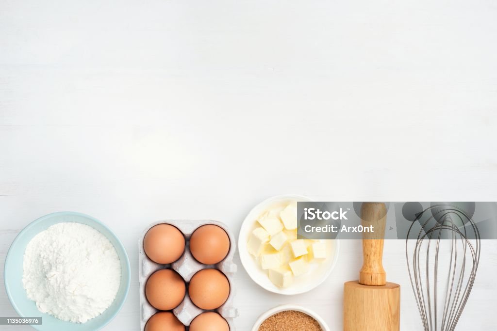 Baking ingredients and kitchen utensils on white background Baking ingredients and kitchen utensils on white background. Chicken eggs, butter, sugar, flour, rolling pin and whisker. Cooking, baking, pastry or cookie dough ingredients Baking Stock Photo