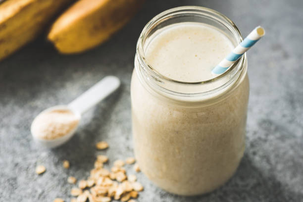 Protein Milkshake With Oats, Banana Protein Milkshake With Oats, Banana in jar with paper drinking straw on concrete background. Closeup view, selective focus. Concept of vegan sporty healthy lifestyle milkshake stock pictures, royalty-free photos & images