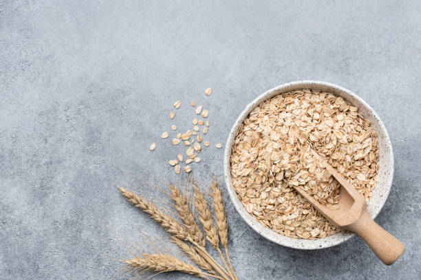 avena enrollada, copos de avena en un recipiente sobre fondo de hormigón - oat wheat oatmeal cereal plant fotografías e imágenes de stock