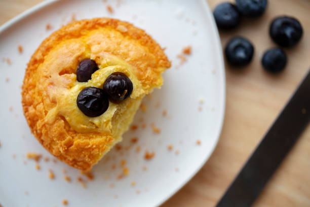 Three muffins stacked on top of each other with blueberries on the bottom. The muffins are topped with blueberries and are sitting on a wooden table