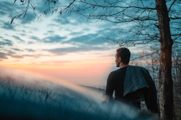 Man parked the car at sunset. Pointing  back and looking at the horizon
