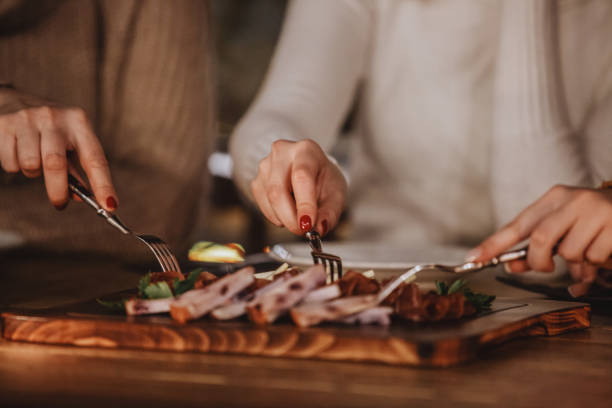 Close-up shot of three women eating delicatessen and cheese at the dining table.