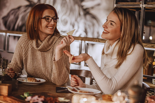 Two joyful women are talking and eating appetizer in a restaurant.