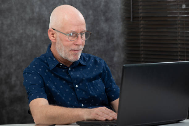 istock senior man with a beard and blue shirt in the office using laptop 1135047940