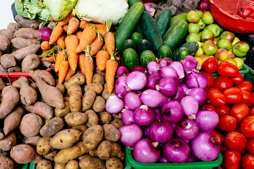 Many market fresh vegetables lined up next to each other in the vibrant colors of a rainbow. Vegetables include; zucchini, broccoli, aubergine, sweet potato radish, red onion, tomato, chili pepper, carrot, bell pepper, onion, garlic, celery, beans and a lemon. Shot from directly above.