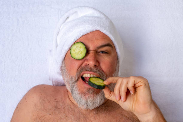 A man with cucumber slices over his eyes makes a funny gesture while receiving a beauty treatment in a salon. stock photo