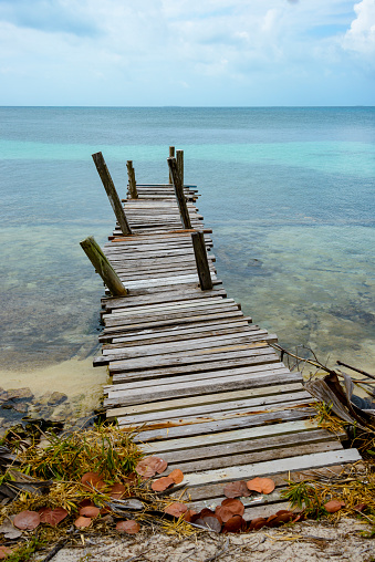 Old dilapidated pier on the shore looking out into the turquoise waters. Belize.