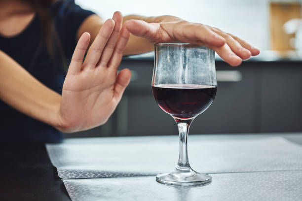 A small step toward recovery is giant progress. Addicted woman refuses to drink a glass of red wine. Close up A glass of red wine standing on the table with female hands on it. Woman refuses to drink alcohol. Kitchen in the background sobriety stock pictures, royalty-free photos & images