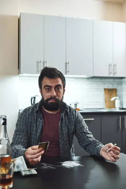 Photo of The false friend of the human mind. Man preparing to snort a line of cocaine with a rolled up bank note. Close up