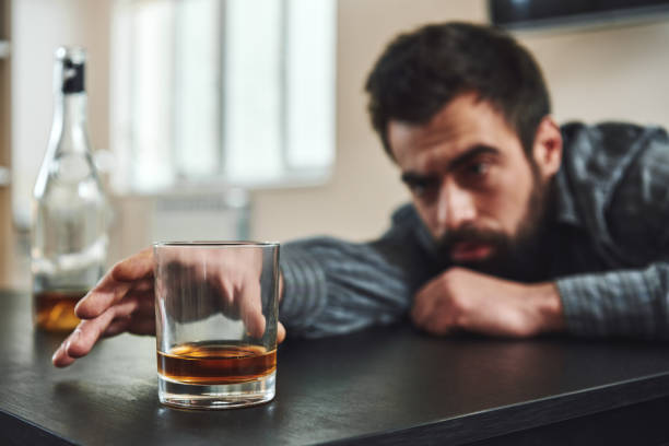 istock You have to break down before you can break through. Alcohol abuse: drunk man lying down on a table looking at a glass of whiskey. Selective focus 1135071215