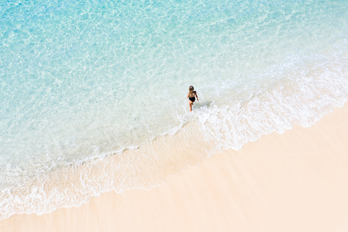 Woman on the white sand beach and transparent turquoise ocean. View from above. Bali island