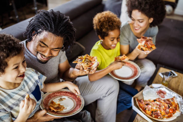 happy african american family eating pizza at home. - pizza eating african descent lunch imagens e fotografias de stock