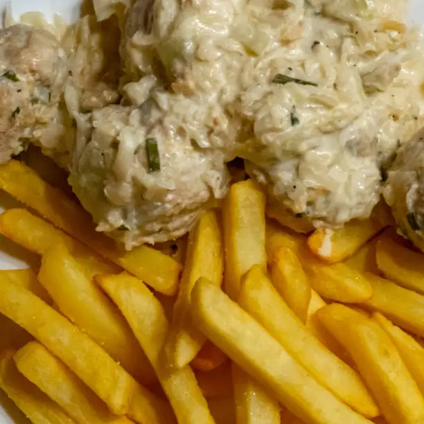 Polish meatballs in cream sauce with celery and spring onions on french fries made from fresh potatoes, homemade fare, food
