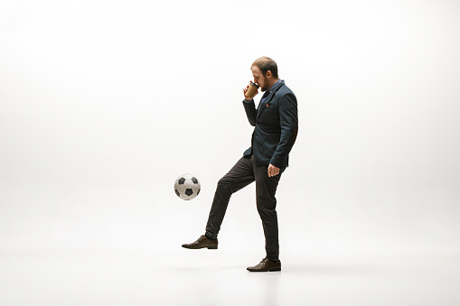 Businessman with a cup of coffee and football ball in office. Soccer freestyle. Concept of balance and agility in business. Manager perfoming tricks isolated on white studio background.