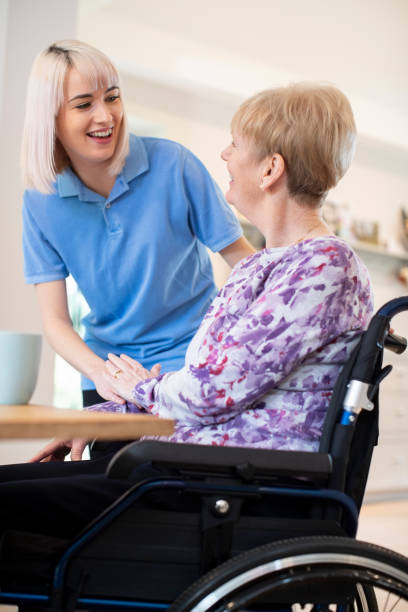 自宅で車椅子に座っている先輩女性に話す女性介護アシスタント - residential care 写真 ストックフォトと画像