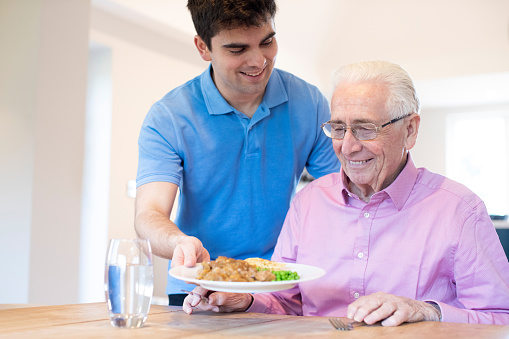 Asistente de cuidado masculino sirviendo comida a Senior masculino sentado en la mesa photo