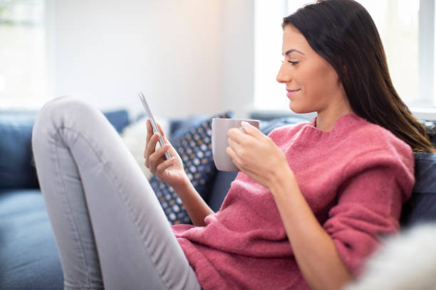 istock Young Woman Relaxing On Sofa With Hot Drink Checking Mobile Phone 1135080764
