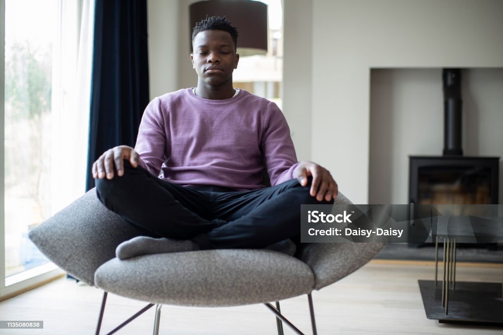 Close Up Of Peaceful Teenage Boy Meditating Sitting In Chair At Home Meditating Stock Photo