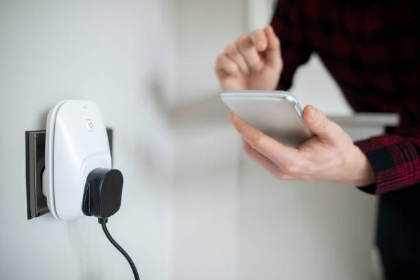 Man Controlling Smart Plug Using App On Mobile Phone Man Controlling Smart Plug Using App On Mobile Phone internet of things photos stock pictures, royalty-free photos & images