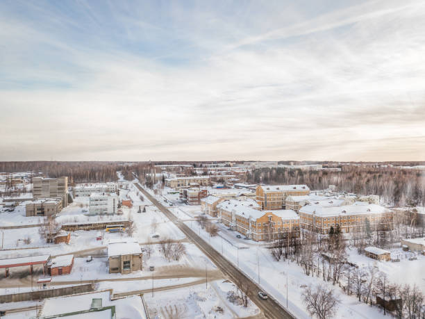 Photo of Winter landscape from a aerial view of the city of Novosibirsk in the haze with streets, small buildings, covered by snow and road crossed at the sunset with blue sky