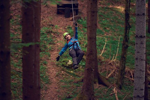 sportive woman with protective equipment in the woodland zip lining.