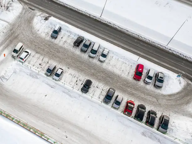 Aerial view of a large number of cars of different brands and colors standing in a parking covered with snow lot near the shopping center in a chaotic manner in the winter day