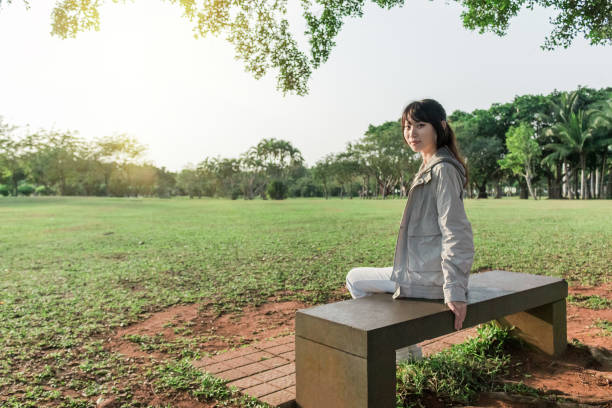 Side View Of Woman Reading Book While Sitting On Bench In Park