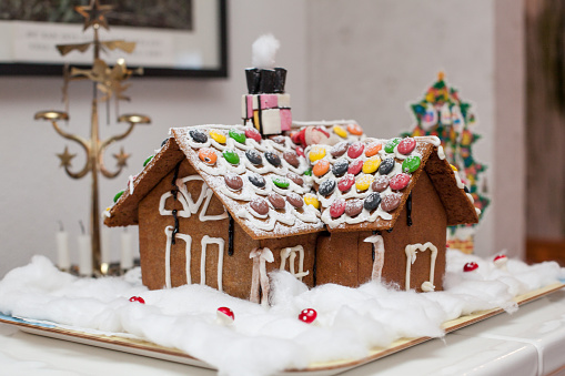 Christmas house made of gingerbread cookies decorated with sugar icing on blue background with bokeh garland.