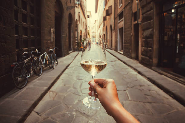 Wine glass in hand of happy tourist walking past historical houses of Florence, Tuscany. Ancient streets in Italy stock photo