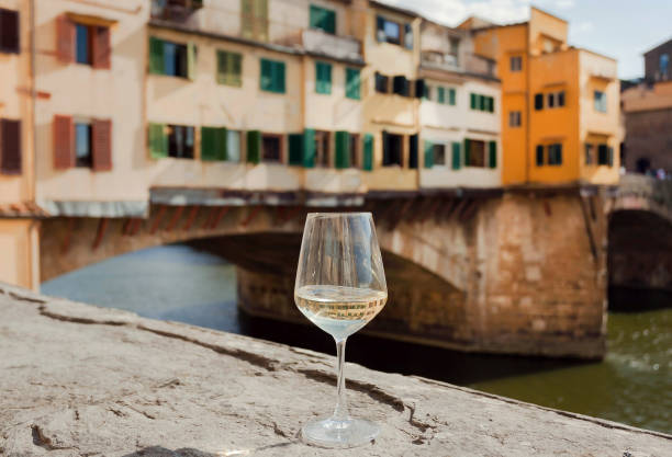 belle journée de voyageur avec verre à vin près des rives de la rivière en italie. matin ensoleillé après le pont ponte vecchio dans florence historique, toscane - sun sunlight italy florence italy photos et images de collection