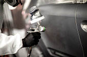 Professional car painter blasting a car segment with a base coat paint in a workshop