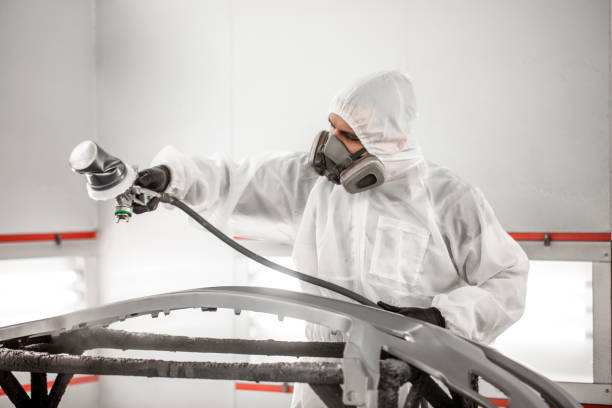 istock Car painter in white overalls spraying a car bumper with paint 1135112518